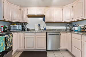 Kitchen featuring light tile patterned floors, stainless steel appliances, a textured ceiling, and dark stone countertops