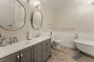 Full bath with light wood-style floors, a freestanding tub, double vanity, wainscoting, and a shower stall