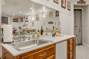 Indoor bar with light countertops, brown cabinetry, white dishwasher, recessed lighting, and light carpet