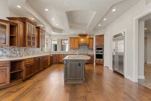 Kitchen with open shelves, glass insert cabinets, cherry wood cabinets, light stone counters, and recessed lighting