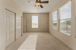 Unfurnished bedroom featuring light colored carpet, a ceiling fan, and a closet