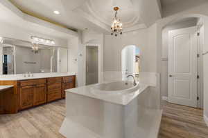 Primary bath with a chandelier, a raised ceiling, vanity, a bath, and light wood-type flooring