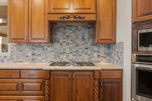 Kitchen featuring decorative backsplash, appliances with stainless steel finishes, cherry wood cabinetry, custom exhaust hood, and light stone counters