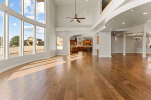 Unfurnished living room featuring arched walkways, ceiling fan, a towering ceiling, light wood-style floors, and recessed lighting