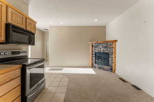 Kitchen with stainless steel electric range oven, black microwave, light colored carpet, light tile patterned flooring, and a fireplace