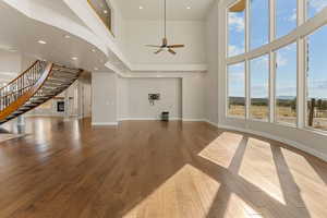 Unfurnished living room with a high ceiling, stairway, wood finished floors, recessed lighting, and ceiling fan