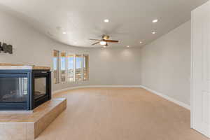 Unfurnished primary suite featuring a tiled fireplace, recessed lighting, light colored carpet, and a ceiling fan