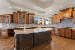 Kitchen featuring open shelves, glass insert cabinets, brown cabinets, backsplash, and light stone counters
