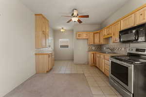 Kitchen with stainless steel electric range, black microwave, light tile patterned flooring, light brown cabinetry, and backsplash