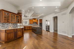 Kitchen featuring cherry wood cabinets, arched walkways, a kitchen island, glass insert cabinets, and tasteful backsplash