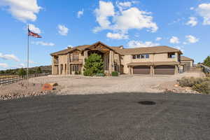 View of front facade featuring gravel driveway, stucco siding, a garage, stone siding, and a balcony