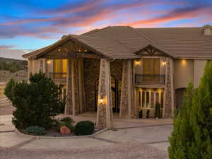 Back of property at dusk with a balcony, stone siding, stucco siding, and driveway