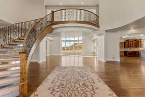 Entrance foyer featuring a towering ceiling, arched walkways, recessed lighting, dark wood-style flooring, and stairs