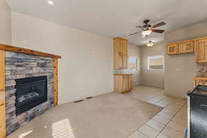 Kitchen with light tile patterned floors, black range, light brown cabinets, a ceiling fan, and a fireplace