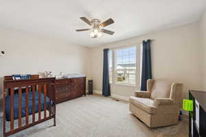 Bedroom with a nursery area, carpet flooring, and a ceiling fan