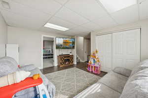 Living area with dark wood finished floors, stairway, a drop ceiling, and a fireplace