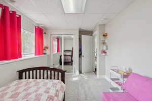Bedroom featuring light carpet, a paneled ceiling, and a closet