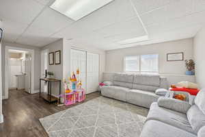Living room with a paneled ceiling and dark wood-style flooring