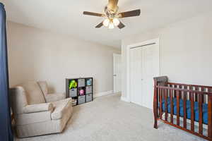 Carpeted bedroom featuring a crib, a closet, and a ceiling fan