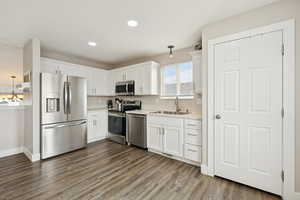 Kitchen with decorative light fixtures, appliances with stainless steel finishes, white cabinets, light countertops, and dark wood finished floors