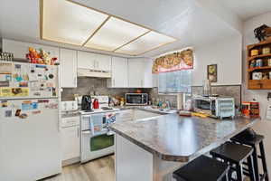 Unit 3 Kitchen with a peninsula, a breakfast bar, white appliances, white cabinetry, and light wood-type flooring