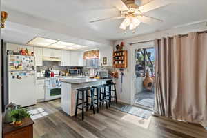 Unit 3 Kitchen with a breakfast bar area, white appliances, white cabinets, light wood-type flooring, and decorative backsplash