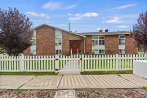 View of front facade featuring brick siding, a chimney, and a fenced front yard