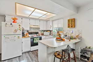 Unit 2 Kitchen with white appliances, decorative backsplash, a kitchen breakfast bar, light countertops, and white cabinets