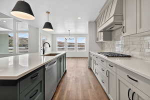 Kitchen with pendant lighting, a chandelier, decorative backsplash, stainless steel appliances, and premium range hood