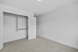 Unfurnished bedroom featuring light carpet and a closet