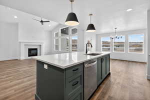 Kitchen featuring hanging light fixtures, vaulted ceiling, stainless steel dishwasher, recessed lighting, and an island with sink