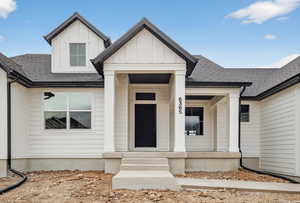 View of exterior entry featuring board and batten siding, roof with shingles, and covered porch