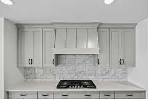Kitchen featuring light stone counters, stainless steel gas stovetop, premium range hood, backsplash, and a textured ceiling