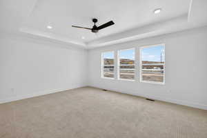 Carpeted empty room with a raised ceiling, recessed lighting, and ceiling fan