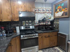 Kitchen with tasteful backsplash, appliances with stainless steel finishes, exhaust hood, and brown cabinetry