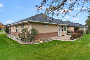 Back of house with brick siding, a patio, a yard, and stucco siding