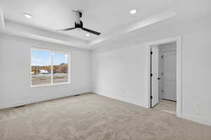 Empty room featuring a raised ceiling, light carpet, ceiling fan, and recessed lighting