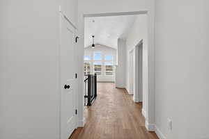 Hall featuring an upstairs landing, vaulted ceiling, and light wood-type flooring