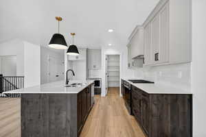 Kitchen featuring dark brown cabinets, stainless steel appliances, a center island with sink, decorative light fixtures, and recessed lighting