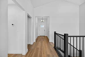 Hallway featuring light wood finished floors, a chandelier, an upstairs landing, and high vaulted ceiling