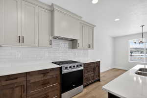 Kitchen with stainless steel gas stove, hanging light fixtures, light wood-style flooring, tasteful backsplash, and a chandelier