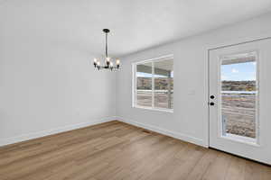 Unfurnished dining area with light wood finished floors, a chandelier, and a textured ceiling