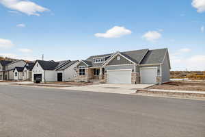 View of front of home with stone siding, roof with shingles, an attached garage, and concrete driveway