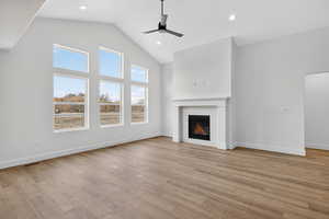 Unfurnished living room with high vaulted ceiling, a glass covered fireplace, a ceiling fan, light wood-type flooring, and recessed lighting