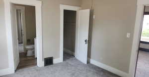 Unfurnished bedroom with light colored carpet, connected bathroom, and a closet
