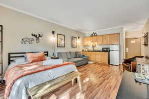 Bedroom with crown molding, freestanding refrigerator, and light wood-style flooring
