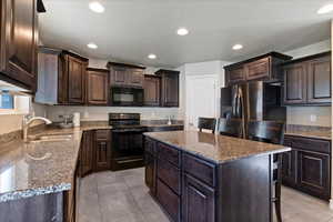 Kitchen featuring black appliances, dark brown cabinets, recessed lighting, a kitchen island, and light stone countertops