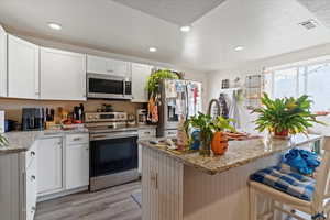 Basement Kitchen featuring appliances with stainless steel finishes, white cabinets, light stone countertops, recessed lighting, and a textured ceiling