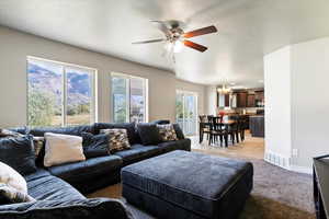 Living room with a textured ceiling, ceiling fan, light carpet, light tile patterned floors, and a chandelier