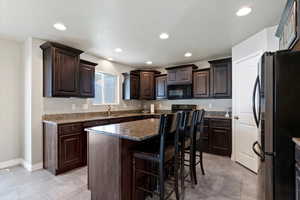 Kitchen featuring dark brown cabinets, black appliances, a breakfast bar area, recessed lighting, and light tile patterned floors
